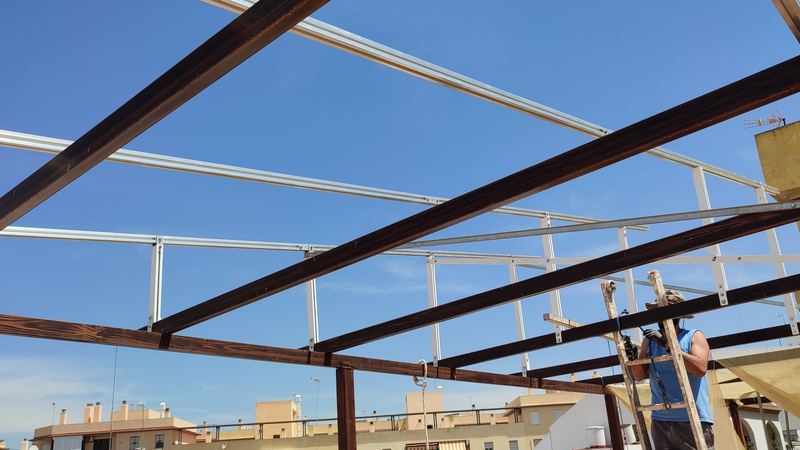Estructura de vigas de madera y correas de aluminio de una pérgola solar en una azotea de Sevilla