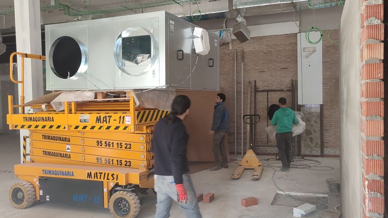 Operarios colocando con plataforma elevadora el climatizador de un local comercial