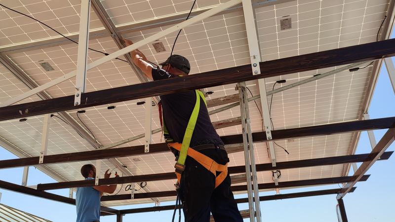 Dos instaladores colocando placas solares bajo la estructura de una pérgola fotovoltaica